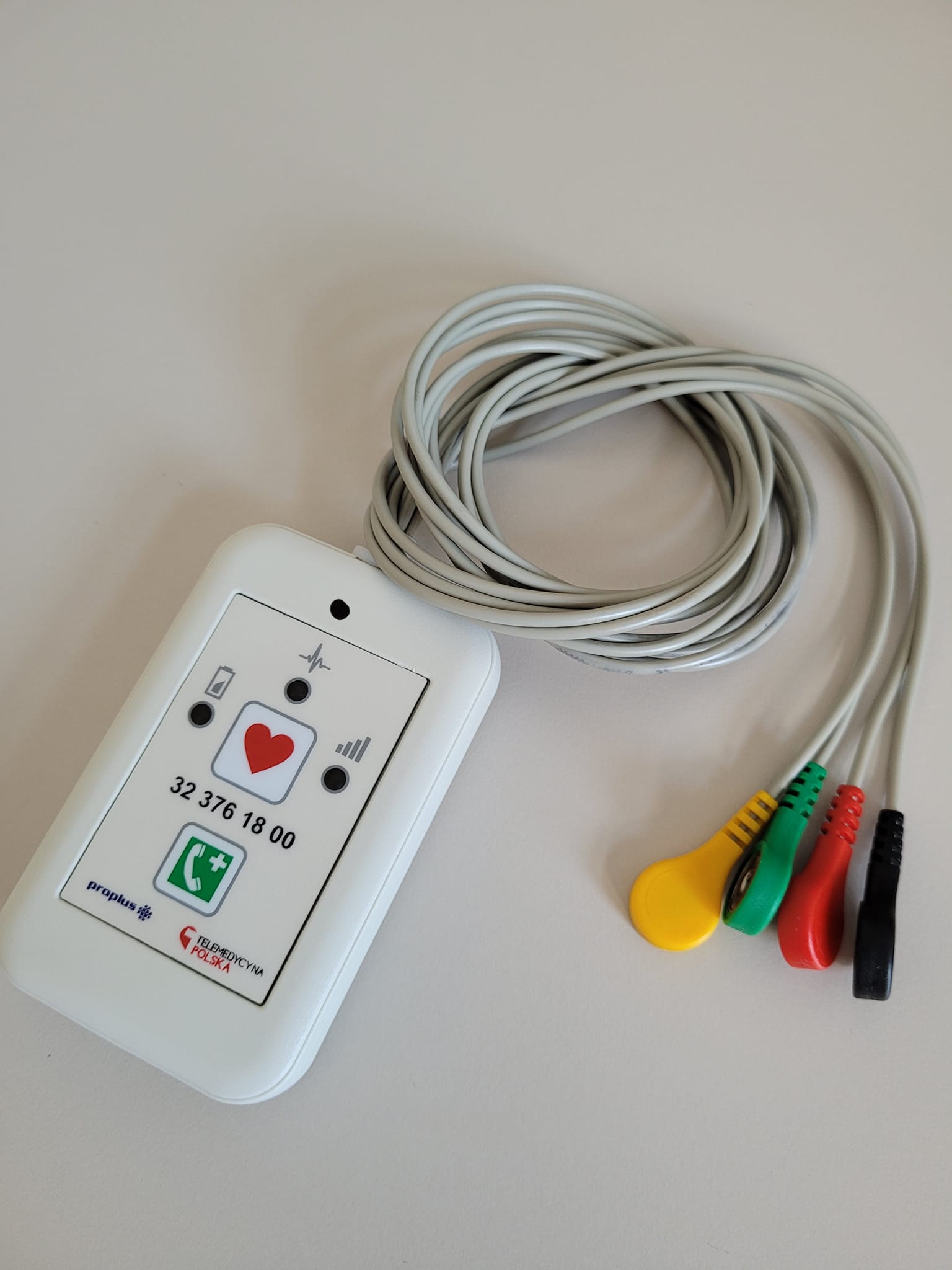 Urządzenie telemedyczne do przedłużonej rejestracji EKG w postaci małego prostokąta z czterema kolorowymi elektrodami.